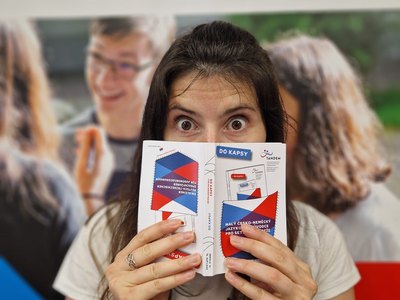 Eine Frau hält den deutsch-tschechischen Sprachführer Do kapsy in der Hand. Im Hintergrund ist ein Roll-Up mit dem Schriftzug Ahoj - Hallo zu sehen.